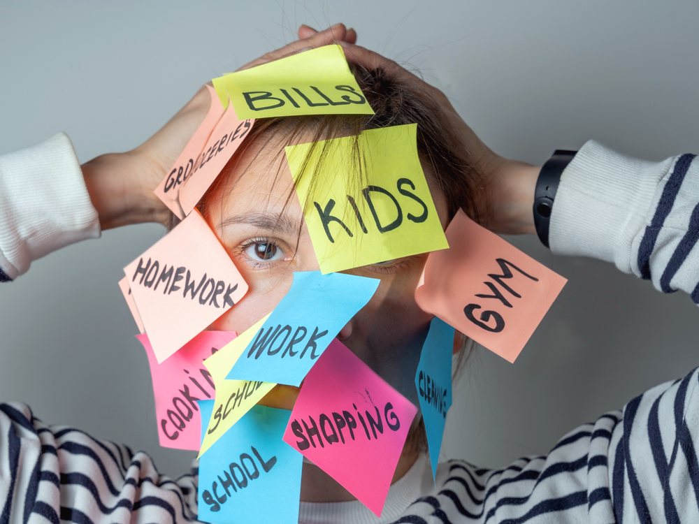 Frau mit vielen Klebezetteln im Gesicht: Kids, Work, School, Shopping – der Kopf ist voll